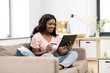 © Syda Productions - internet banking, online shopping and technology concept - happy smiling african american woman sitting on sofa with tablet pc computer and credit card at home