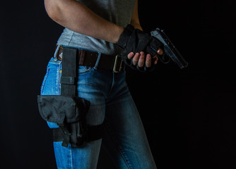 A girl with a view from waist to mid thigh with a holster on her leg holds a gun in her hands