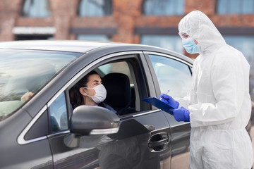 Wall Mural - medicine, quarantine and pandemic concept - doctor or healthcare worker in protective gear or hazmat suit, medical mask, gloves and goggles with clipboard and woman in car waiting for coronavirus test