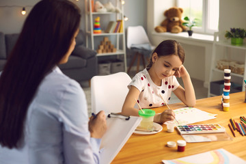 Child psychologist. A woman psychologist with a clipboard works with a little girl patient in a children's room.