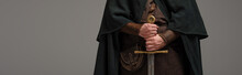 Cropped View Of Medieval Scottish Knight In Mantel With Sword In Hands On Grey Background, Panoramic Shot