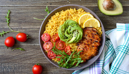 Wall Mural - Bulgur with grilled chicken breast, fresh vegetables, avocado, arugula. Diet lunch on a wooden table. Healthy food. Top view.