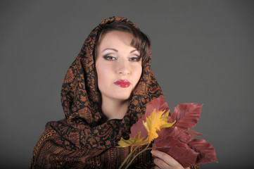 beautiful Russian brunette woman with a scarf on her head and autumn leaves in her hands