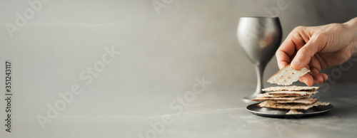 Fotografía Hands with chalice and communion matzo bread, wooden cross on grey background