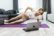 © F8  \ Suport Ukraine - Young woman exercising at home in a living room. Video lesson. Young woman repeating exercises while watching online workout session.
