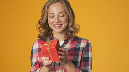 Wall Mural - Young cheery girl isolated over yellow wall background holding present box trying to guess what's inside