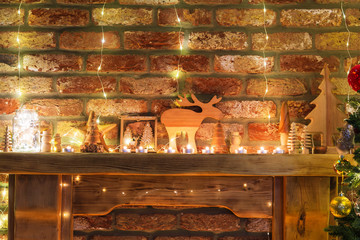 Wall Mural - Beautiful decorated fireplace, wooden mantelpiece with fairy lights, handmade ornaments, candles and lantern, Christmas tree to the side, selective focus