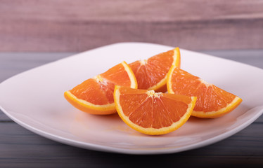 Slices orange fresh juicy oranges on white dish,  wood background.