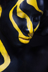 Wall Mural - Woman with black body paint. Cheerful young african girl with art bodypaint. An amazing model with yellow makeup. Closeup face.