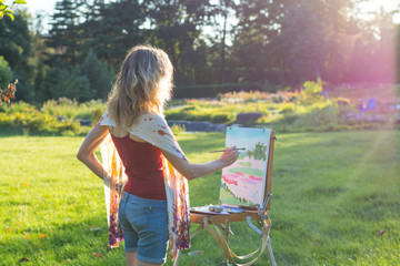 The painter paints oil paintings in the garden at sunset