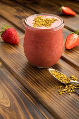 Wall Mural - Smoothies with strawberry  and  bee pollen in the small glass jar on the brown  wooden background.  Location vertical.