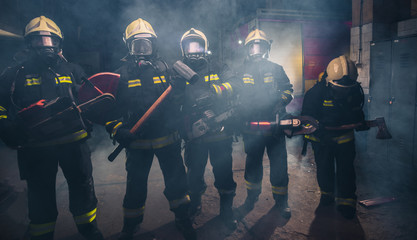 Wall Mural - Group of firefighters with  chainsaw and sledge hammer practicing in the garage of the fire department