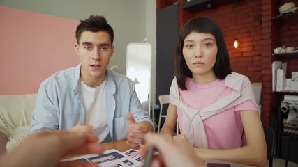 Wall Mural - POV shot of two diverse young designers presenting printouts with application interface templates for different devices to you as client sitting at desk in office