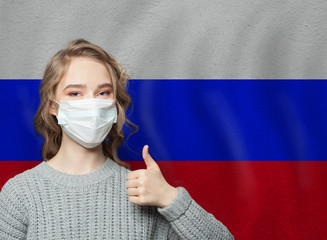 Wall Mural - Happy woman in face mask holding thumb up on Russian flag background. Flu epidemic and virus protection concept