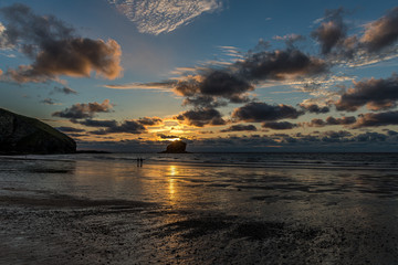 Two people paddling at low tide, watching the sunset behind Gull Rock, Portreath, Cornwall