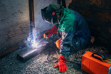 A Welder Welds A Metal Pole With Electric Welding, Holds An Electrode In His Hands