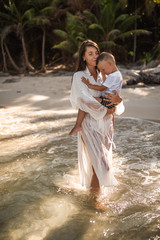 Wall Mural - Happy smile european family have rest and run on white sand beach. Father, long black chestnut hair mother, blond baby boy. white cotton clothes. boho dress. t-shorts.Thailand. Aquamarine crystal sea