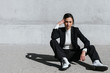 © Westend61 - Young woman wearing black suit sitting on floor in front of concrete wall