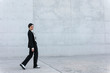 © Westend61 - Young woman wearing black suit walking in front of concrete wall