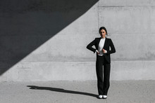 Young Woman Wearing Black Suit Standing In Front Of Concrete Wall