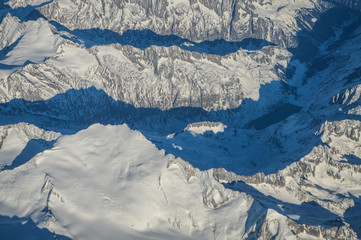 View over the clouds from the porthole of an airplane of swiss alps mountains