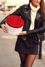 Outdoor Portrait Of Young Beautiful Woman Holding White Box With Red Roses, Wearing Leather Jacket