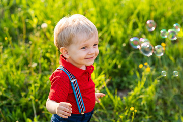 child boy has fun playing in nature with shiny soap bubbles