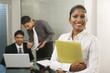 © ImageHit - Businesswoman holding folder, businessmen discussing in the background