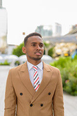 Wall Mural - Happy young handsome African businessman thinking in the city streets