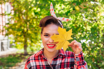 beautiful woman with make up and hair in pin up style standing on the street, holding yellow maple l