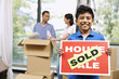 © ImageHit - Boy holding For Sale sign with SOLD on it, man and woman packing in the background