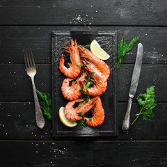 Wall Mural - Boiled shrimp with parsley and lemon on a black stone plate. Top view. Seafood.