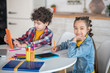 © zinkevych - Boy and girl sitting at round table with tablets, busy with their assignments, girl smiling into the camera
