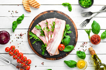 Wall Mural - Slices of bacon with arugula and parsley on a black plate. Top view. Free space for your text.