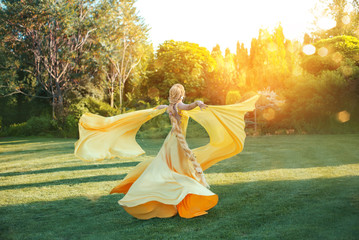 bright divine sun light. Art Fantasy happy woman dancing spinning hand raised yellow silk dress, cape train fluttering fly in wind. Blonde girl hairstyle long braid. Princess rapunzel back rear view