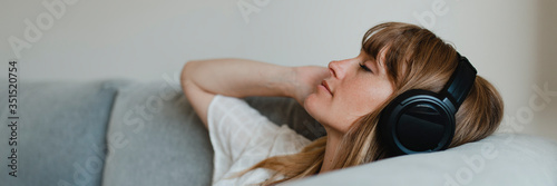 Woman listening to music during coronavirus quarantine on a couch Poster Mural XXL
