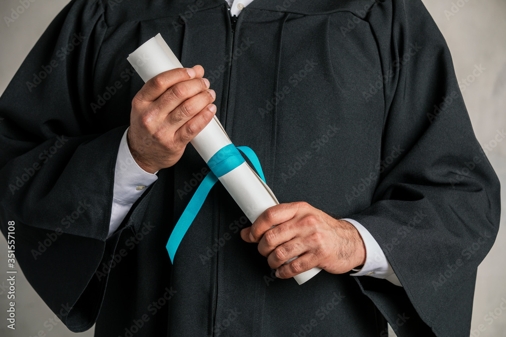 Student in a graduation gown holding his diploma Stock Photo | Adobe Stock
