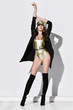 © Dmitry Lobanov - Young beautiful brunette woman in golden swimsuit, cap, black high boots and jacket standing over white wall full body