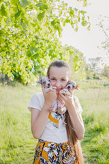 Happy beautiful girl holding two little  puppies in her arms (American Hairless Terrier). Beautiful background of green grass and trees.Children and dogs concept. Place for text.