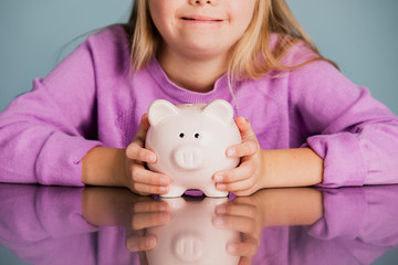 Cute little girl with Down Syndrome saving money in a piggy bank