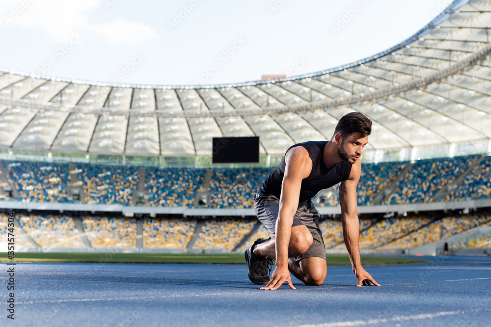handsome runner in start position on running track at stadium - obrazy, fototapety, plakaty 