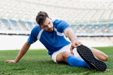 Wall Mural - selective focus of professional soccer player in blue and white uniform stretching on football pitch at stadium