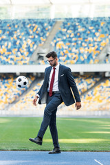 Wall Mural - young businessman in suit and glasses playing with soccer ball at stadium