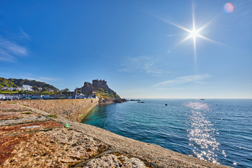Wall Mural - Image of the back of the pier of Gorey Harbour with Gorey Castle in the background with a clam sea, sunshine with a blue sky taken early morning. Jersey,Channel Islands, UK