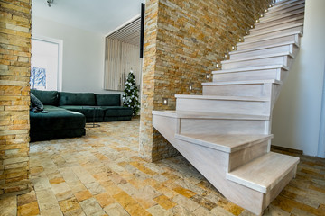 Stylish wooden contemporary staircase inside loft house interior. Modern hallway with decorative limestone brick walls and white oak stairs.