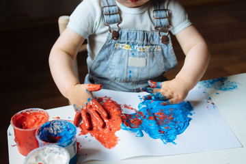 Child painting with her hands on the table at home using blue and red paint. Finger painting or art therapy for children. Fun activities for toddlers. Close up.  