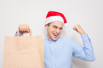 Wall Mural - Man in Santa Claus hat screaming: Yes! Man is happy to receive a gift bag, portrait, white background, copy space. Concept of Christmas shopping