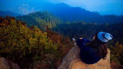 A girl sits on the edge of the cliff and looking at the valley and mountains