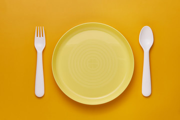 Plastic white cutlery set with yellow background. Top view