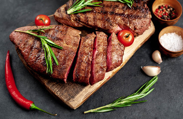 Tasty two grilled beef steaks with spices and herbs on a cutting board on a stone background